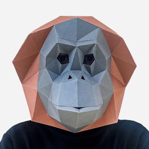 May include: A papercraft mask of an orangutan, with a brown and gray color scheme. The mask is made of folded paper and has a realistic design.