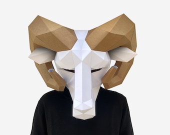 Może przedstawiać: Biało-brązowa maska barana z papier-mache z dużymi rogami. Maskę nosi osoba w czarnej koszuli.