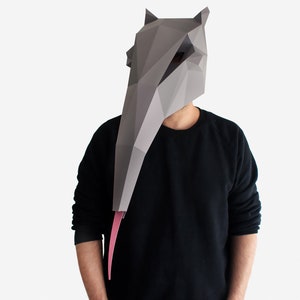 May include: A person wearing a gray paper mache mask shaped like an anteater with a pink tongue. The mask covers the person's entire face and head. The person is wearing a black long-sleeved shirt.