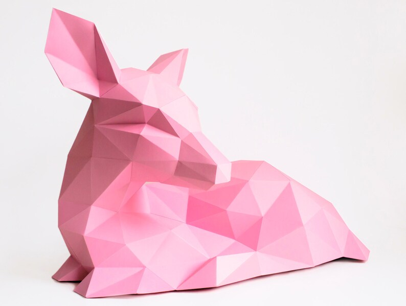 May include: A pink origami deer sculpture with a geometric design. The deer is lying down with its head resting on its front legs.