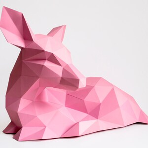 May include: A pink papercraft deer sculpture in a lying down position. The deer is made of folded paper and has a geometric design.