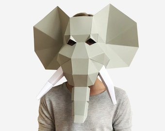 May include: A gray papercraft elephant mask with white tusks. The mask is worn by a person, but the person's face is not visible.