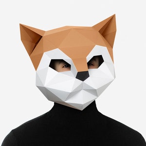 May include: A person wearing a brown and white origami fox mask. The mask is made of paper and has a geometric design.