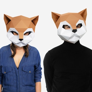 May include: Two people wearing paper mache animal masks. The masks are brown and white and shaped like a fox's head. One person is wearing a blue denim shirt and the other is wearing a black turtleneck.