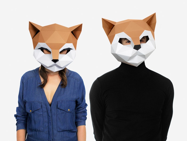 May include: Two people wearing paper mache animal masks. The masks are brown and white and shaped like a fox's head. One person is wearing a blue denim shirt and the other is wearing a black turtleneck.