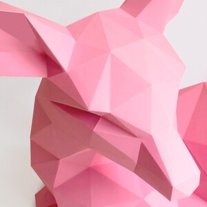 May include: A pink origami deer sculpture with a geometric design. The deer is lying down with its head turned to the side.