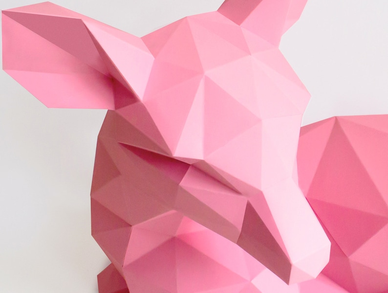 May include: A pink origami deer sculpture with a geometric design. The deer is lying down with its head turned to the side.