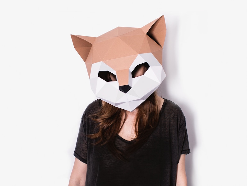 May include: A person wearing a brown and white papercraft fox mask. The mask is made of folded paper and has a realistic design. The person is wearing a black shirt.
