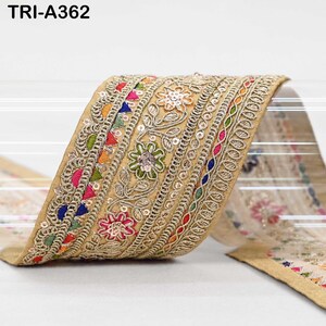 May include: A decorative fabric trim labeled TRI-A362, featuring a gold base with intricate embroidery in floral patterns. The design includes multi-colored thread accents in pink, blue, green, and orange, embellished with small reflective sequins.