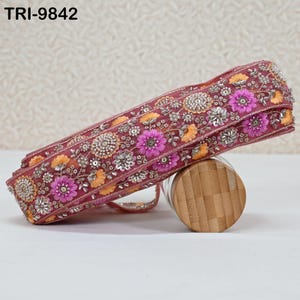 May include: A decorative burgundy ribbon with intricate floral embroidery in shades of pink, orange, and silver. The ribbon is embellished with beads and sequins, and the text "TRI-9842" is visible.
