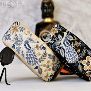 May include: Two rolls of embroidered fabric trim, one beige and one black, featuring a repeating pattern of blue peacocks, light blue leaves, and tan flowers. The rolls are labeled #1 and #2, with the text GTR1394-A visible in the top corner.