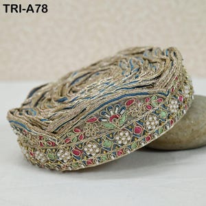 May include: A roll of decorative trim with intricate embroidery. The trim features gold, blue, red, green, and white floral patterns. The text "TRI-A78" is visible in the upper left corner. The trim is likely used for embellishing clothing or crafts.
