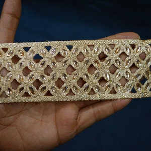 May include: A gold-colored decorative trim featuring a repeating floral pattern constructed from metallic thread and embedded with clear, marquise-shaped crystals. The band has a structured, open-work design with a consistent width throughout.
