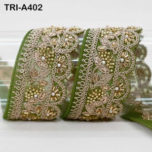 May include: A roll of olive green fabric trim featuring an intricate scalloped edge, embroidered with gold metallic thread in a floral pattern, and embellished with small clear beads and white pearls. The text TRI-A402 is visible at the top.