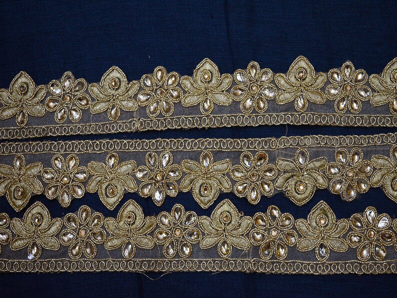 May include: Three strips of gold-toned decorative trim featuring a repeating floral pattern. Each flower is crafted with metallic gold thread embroidery and accented with clear, teardrop-shaped crystals set within the petals on a sheer mesh base.