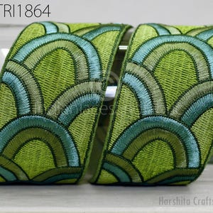 two pieces of embroidered fabric with a repeating pattern of green and blue waves or circles. The fabric appears to be a decorative textile, possibly used for clothing or home decor.