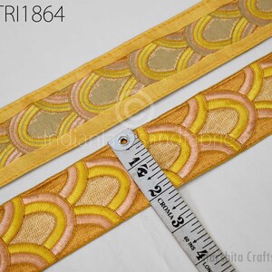 a close-up view of a decorative fabric with a repeating pattern of yellow and orange circles, and a ruler is placed next to it to measure the length of the fabric.