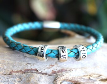 May include: A turquoise leather bracelet with three silver beads, each engraved with a name: "Emma", "Ash", and "Olivia".