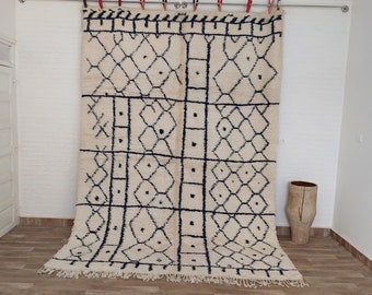 May include: A white and black Moroccan rug with a geometric pattern. The rug is hanging on a wall with a white background.