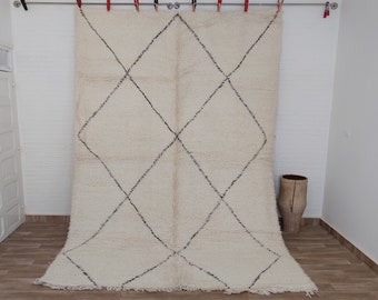 May include: A white Moroccan rug with a diamond pattern in black. The rug is hanging on a wall with clothespins.