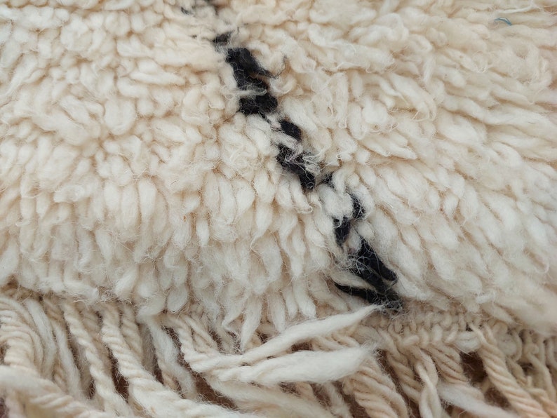 Authentic Beni Ourain Moroccan rug in cream handwoven wool with black diamond lattice, fringed edges on a 5x9 area rug.