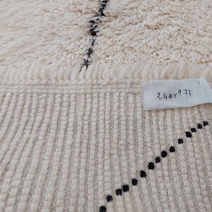 Authentic Beni Ourain Moroccan rug in cream handwoven wool with black diamond lattice, fringed edges on a 5x9 area rug.