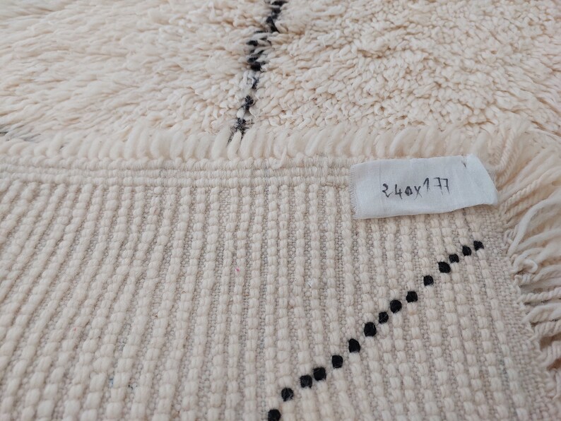 Authentic Beni Ourain Moroccan rug in cream handwoven wool with black diamond lattice, fringed edges on a 5x9 area rug.