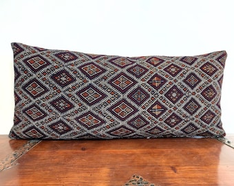 May include: A long, rectangular pillow with a dark blue background and a geometric pattern in shades of red, orange, and white.