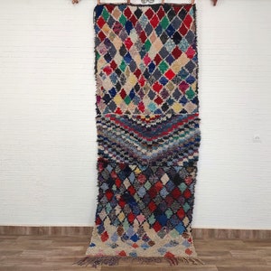 Peut inclure: Un long tapis marocain coloré avec un motif en losanges. Le tapis est en laine et a une frange en bas.