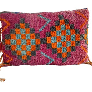 Peut inclure: Un coussin de décoration rose, orange, bleu et gris avec des glands. Le coussin est fait d'un tissu doux et tissé.