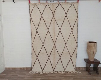 May include: A white and brown Moroccan rug with a diamond pattern. The rug is hanging on a white wall.