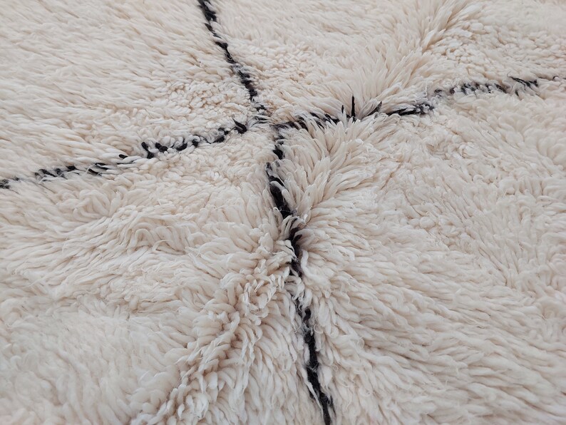 Authentic Beni Ourain Moroccan rug in cream handwoven wool with black diamond lattice, fringed edges on a 5x9 area rug.