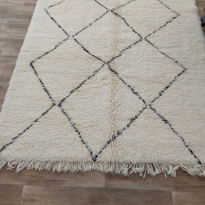 Authentic Beni Ourain Moroccan rug in cream handwoven wool with black diamond lattice, fringed edges on a 5x9 area rug.