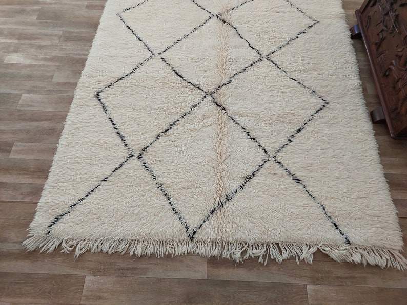 Authentic Beni Ourain Moroccan rug in cream handwoven wool with black diamond lattice, fringed edges on a 5x9 area rug.