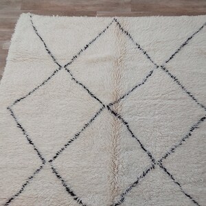 Authentic Beni Ourain Moroccan rug in cream handwoven wool with black diamond lattice, fringed edges on a 5x9 area rug.