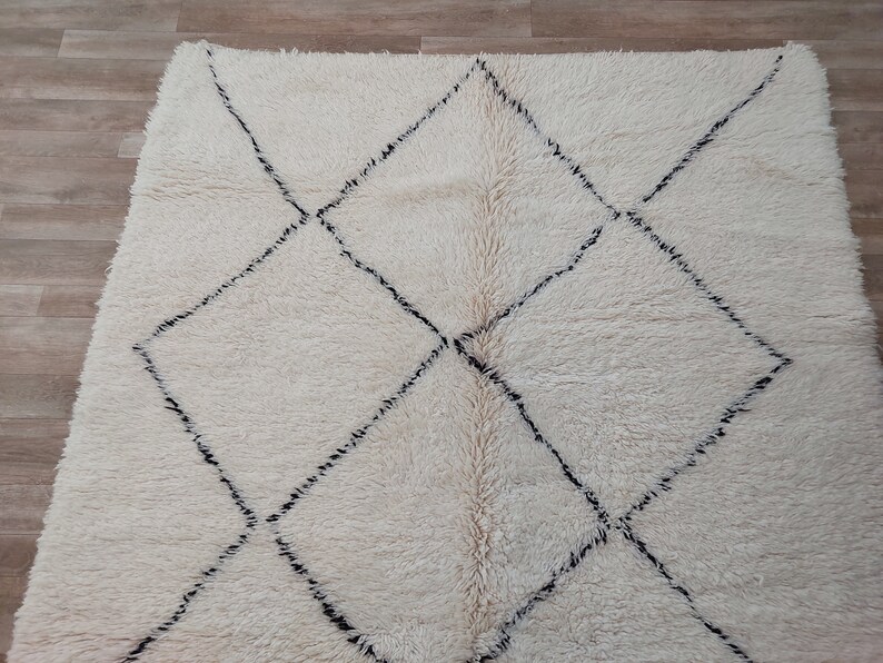 Authentic Beni Ourain Moroccan rug in cream handwoven wool with black diamond lattice, fringed edges on a 5x9 area rug.