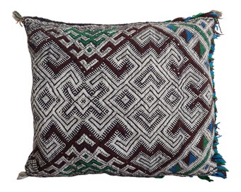 May include: A square throw pillow with a geometric pattern in shades of brown, white, green, and blue. The pillow has a fringe border.