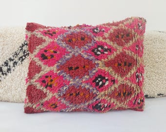 Può includere: Un cuscino decorativo rosa e rosso con un motivo geometrico. Il cuscino è realizzato in tessuto morbido e tessuto e ha un bordo con frange.