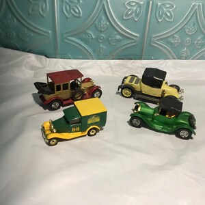 May include: Four miniature vintage car models in various colors. The models include a red and gold car with a roof, a yellow and black convertible, a green and yellow delivery truck, and a green convertible.