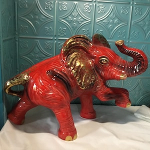 May include: A red ceramic elephant figurine with gold accents. The elephant is standing on all four legs with its trunk raised.