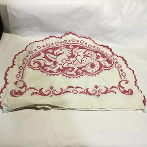 May include: A white, semi-circular embroidered textile with a red floral and animal design. The border is scalloped with a red trim. The embroidery features a central design of two mythical creatures and floral patterns.