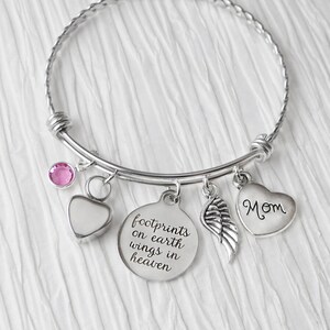May include: Silver charm bracelet with a pink crystal, a heart charm with the word "Mom", a wing charm, and a round charm with the text "Footprints on earth wings in heaven".
