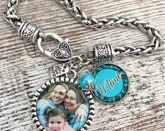 May include: Silver-toned bracelet with a braided chain design. The bracelet features a heart-shaped clasp and several charms, including a round charm with a family photo, a charm that says "You are loved", and a turquoise charm that says "Mimi".