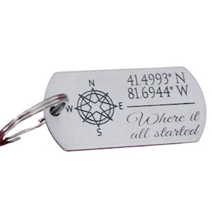 May include: Silver-colored metal keychain tag with a compass design and the text "41.4993° N 81.6944° W Where it all started." The tag has a rounded rectangular shape and a silver key ring.