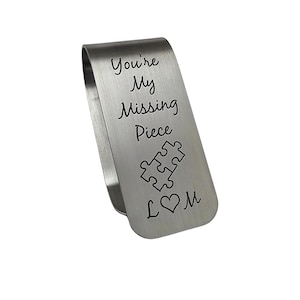 May include: Silver metal bookmark with the text "You're My Missing Piece" and a puzzle piece graphic. The bookmark also has a heart and the letters "L" and "M" engraved on it.