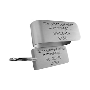 May include: A silver-colored metal keychain with two rectangular tags. The tags have the engraved text "It started with a message... 10-25-15 2:30". One tag is attached to a key ring.