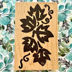 May include: A wooden block stamp with a black floral design. The design features a cluster of stylized leaves with a swirling vine.