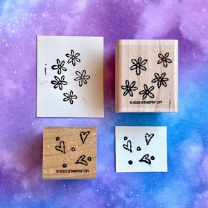 May include: Four wooden blocks with black ink designs. Two blocks have a design of flowers, one block has a design of hearts, and one block has a design of hearts and dots. The blocks have the text "2003 STAMPIN UPI" printed on the bottom.