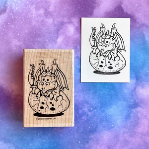 May include: A wooden rubber stamp with a black and white illustration of a dragon hatching from an egg. The text "© 2002 STAMPIN' UP!" is printed on the bottom of the stamp.