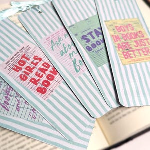 May include: A collection of striped bookmarks with various text designs. The bookmarks have a light blue and white striped pattern. Each bookmark features a different phrase, including "Hot Girls Read Book" and "Boys in Books Are Just Better."